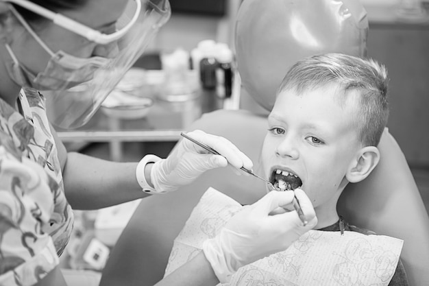 치과 클리닉에서 치과 의사의 리셉션에서 어린 소년. 어린이 치과, 소아 치과. Blac 및 흰색 복고 스타일 사진. 구강 건강 및 위생