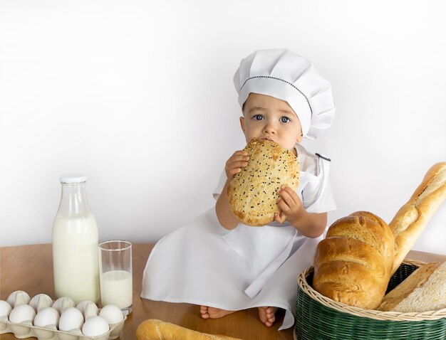 写真 アプロンとキャップをかぶった小さな男の子がパンを調理しテーブルに座っている食料粉製品作物の穀物