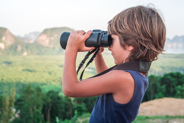 写真 上から暗いtシャツを着た小さな男の子が、野生生物を双眼鏡で遠くから見ています。