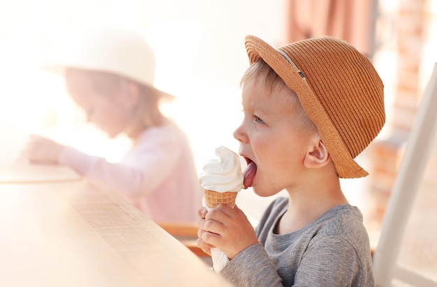 사진 모자를 쓴 어린 소년이 화창한 날 그늘에서 아이스크림을 먹고 있다
