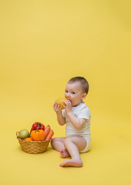 野菜と果物のバスケットを持った少年が黄色い空間に。子供はレモンを見て食べます。垂直方向。コピースペース