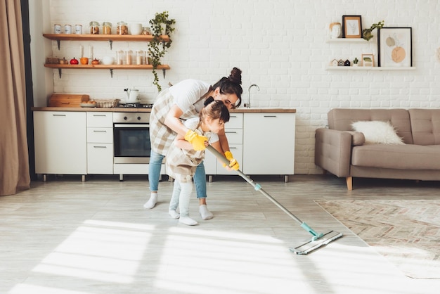 Фото Маленькая дочка и ее мама убирают дом ребенок моет пол на кухне милая маленькая помощница моет пол шваброй счастливая семья убирает комнату