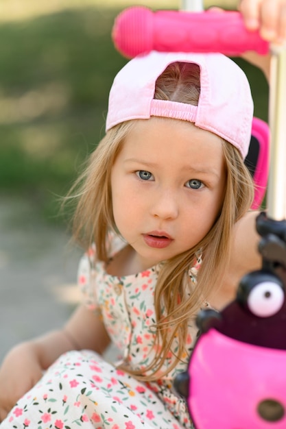 사진 분홍색 모자를 쓴 3살 어린 소녀가 여름 시간에 스쿠터를 탄다
