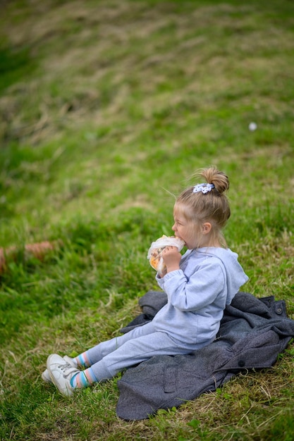 사진 3살 된 어린 소녀가 공원의 잔디밭에 정장을 입고 앉아 피자를 먹습니다