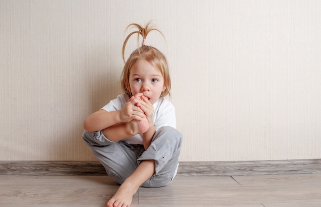 Фото Маленькая девочка кусает ногти на ногах, сидя на полу в комнате у стены. вредные привычки у детей.