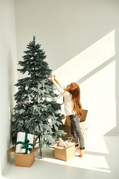 Фото Маленькая девочка украсила елку на белой стене