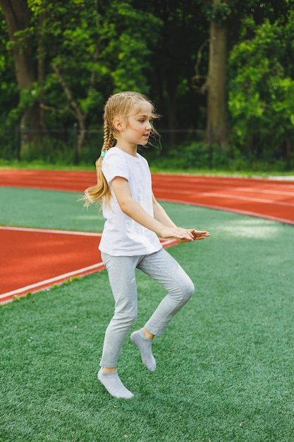 写真 小さな女の子が芝生の上でスポーツに参加します子供はスタジアムでトレーニングする前にウォーミングアップを行います子供のスポーツと健康的なライフスタイル