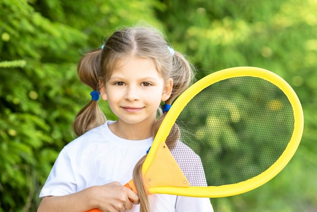 写真 小さな女の子が子供のテニスラケットを持っています