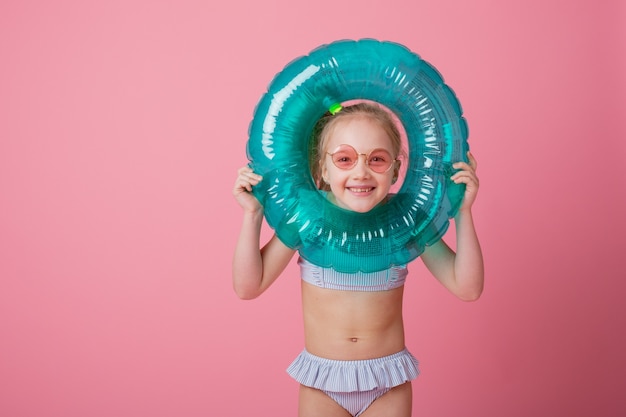 Маленькая девочка в купальнике с плавательным кругом на розовом фоне