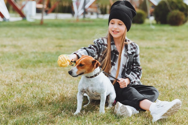 写真 小さな女の子が公園の芝生で犬と遊んでいる ジャック ラッセル テリアの子供が犬におもちゃを与える