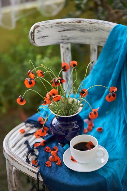 A Little Red Poppies Bouquet in blauwe vaas op vintage stoel. Papavers en kopje koffie.