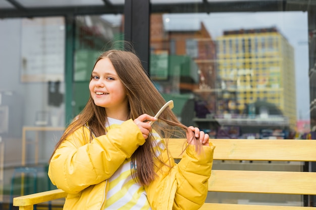 写真 髪の長い陽気なブロンドの女の子が櫛で髪をとかし、不注意に笑います。