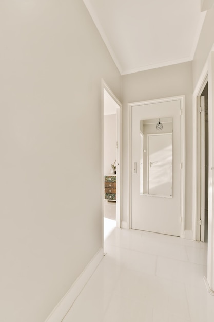 Фото Длинный коридор с белыми стенами и полом, справа открытая дверь, ведущая в другую комнату на другой стороне.