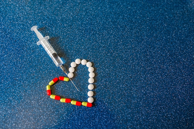 治療の象徴として青い背景に注射されたハート型の錠剤と注射器がたくさん。 covid-19からのワクチンに対する抗生物質の選択。心臓発作の場合の緊急援助