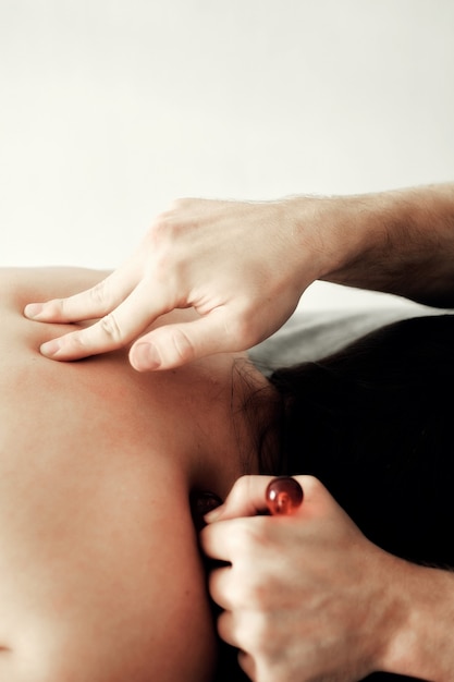 Фото Мужчина-массажист проводит спа-процедуры с помощью специального массажного ролика для молодой женщины, которая лежит