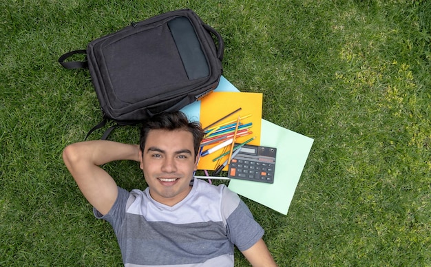 Фото Студент-мужчина лежит на траве с рюкзаком и школьными принадлежностями