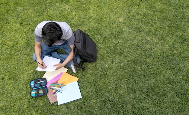 写真 草の上に座ってノートブックに書いている男性学生