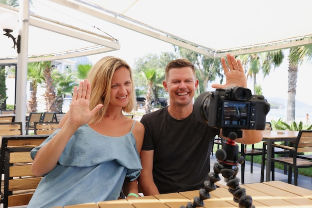 写真 男と女がストリートカフェで三脚に乗ってカメラに手を振る旅行vlog家族旅行