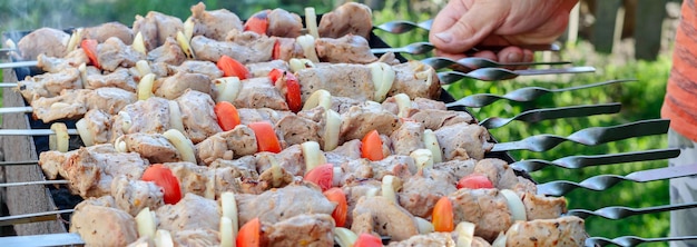 남자는 그릴에 철 꼬치에 야채와 함께 고기를 튀긴다 피크닉 테마에 대한 시시 케밥 배너 요리