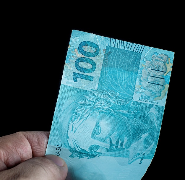 写真 黒の背景にブラジルレアルであるブラジルのお金の100の請求書を保持している男