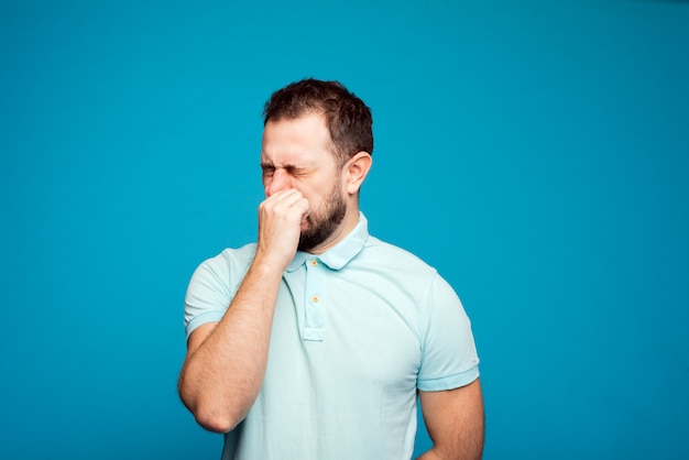 写真 青い背景に青いtシャツを着た男性がくしゃみをします。アレルギーの概念。アレルギー薬を服用する