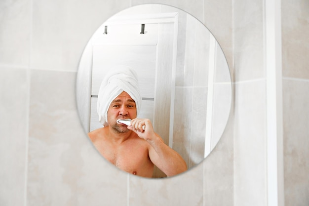 사진 머리에 수건으로 만든 터번을 쓴 남자가 아침 샤워 후 이를 닦는다