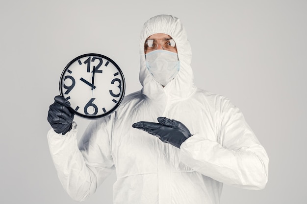 손에 시계가 있는 흰색 배경에 흰색 보호복을 입은 남자 전염병 전염병은 빠르게 확산되는 새로운 바이러스 의료 개념입니다