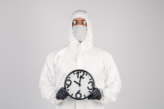 사진 흰색 보호복을 입은 남자, 손에 시계를 들고 흰색 바탕에 마스크를 쓴 남자 전염병 전염병은 빠르게 퍼지는 새로운 바이러스의 의학 개념이다