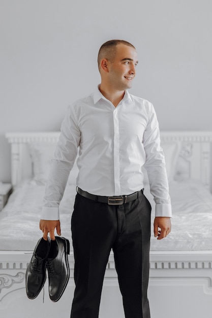 Фото Мужчина в белой рубашке и черных брюках держит пару ботинок