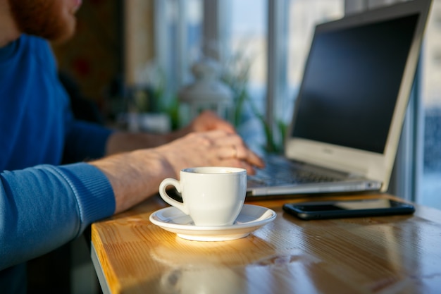 写真 男は一杯のコーヒーの隣のラップトップに座っています