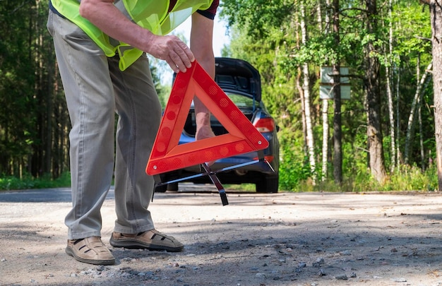 写真 男性が車の近くの道路の横に持ち運べる反射的な赤い三角形の警告三角形を置く