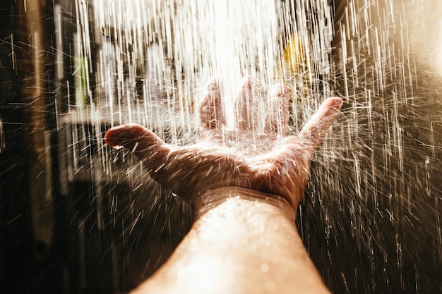 Фото Мужская рука в брызгах воды в солнечном свете на темном фоне.