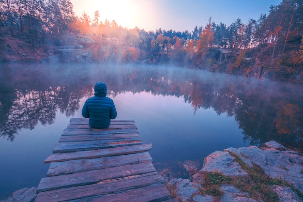 사진 나무 갑판에 앉아 화강암 해안과 호수를 바라 보는 남자. 호수 위에 일출