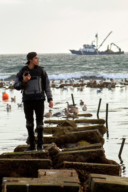 사진 백그라운드에서 보트와 물에 있는 바위에 서 있는 남자.