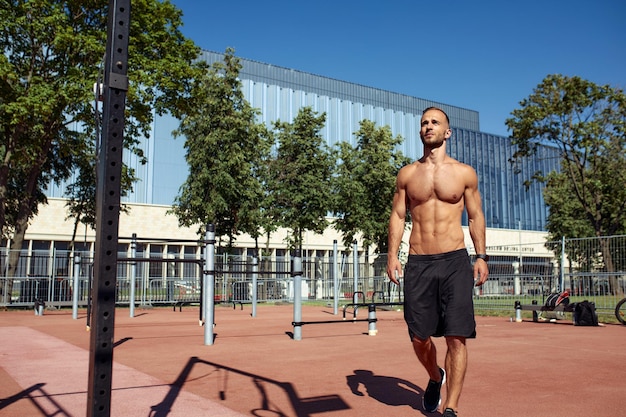 男は彼の体と健康について考える 公園のスポーティな体格のスポーツ スタジアムの肖像画 短い髪のひげ裸の胴体 晴れた夏の日 白人の外観