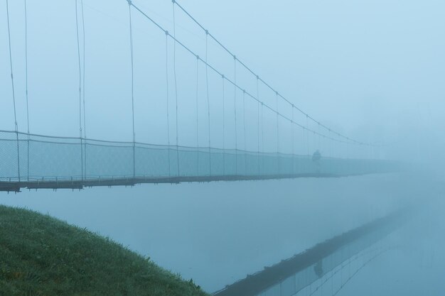 Фото Мужчина идет по подвесному мосту через реку в сильном тумане