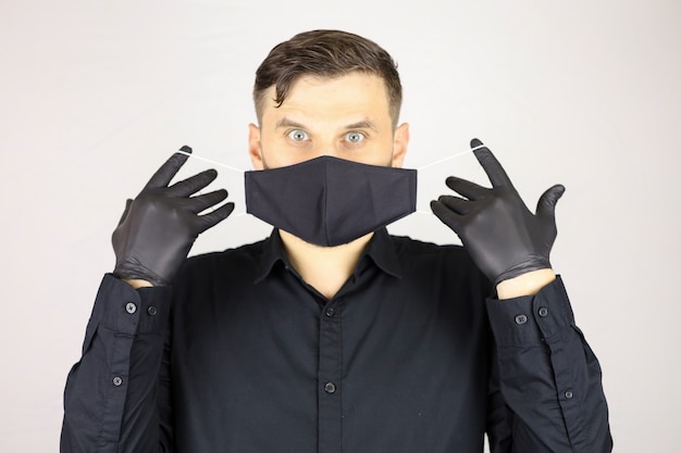 Фото Мужчина в черных медицинских перчатках снимает защитную маску на белом фоне