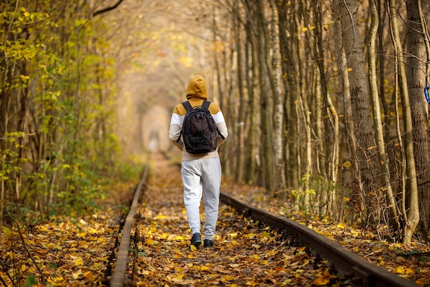 写真 大きなリュックサックを背負った男が線路を進む恋の秋の森トンネルの線路