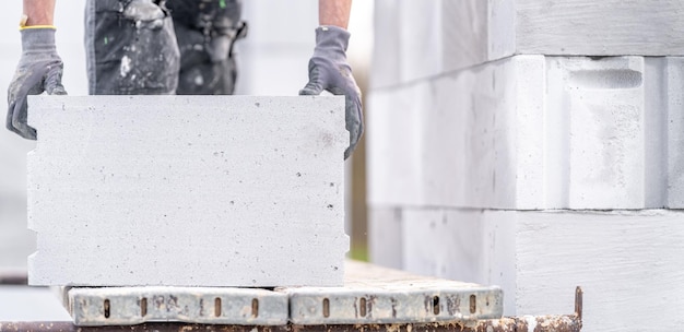 Фото Каменщик строит стену дома из бетонных кирпичей