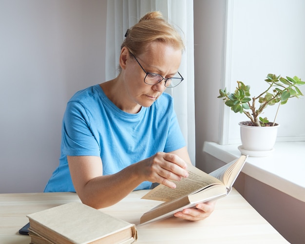 Фото Зрелая женщина читает в очках книгу, листает страницы, пенсионерка учится, получает новые знания