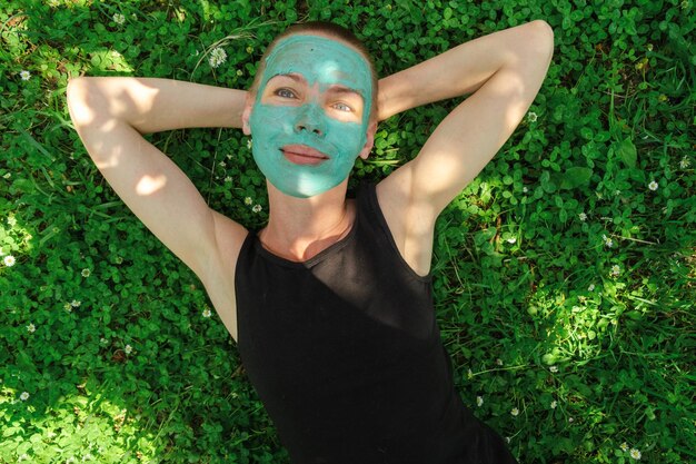 写真 化粧マスクをした中年女性が緑の草の上に横たわる ショートヘアの女性