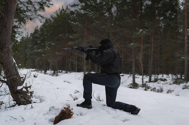 写真 冬の森で膝をかがめて座っている兵士が近代的な突撃ライフルを持って狙いを定めています
