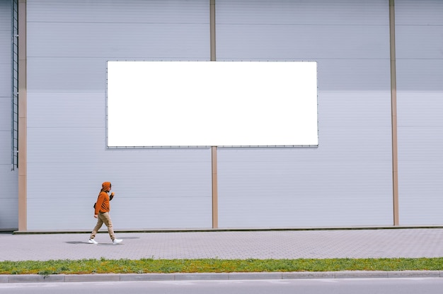 写真 通りを歩いている男性と一緒に灰色の壁に向かって通りの看板のモックアップ。