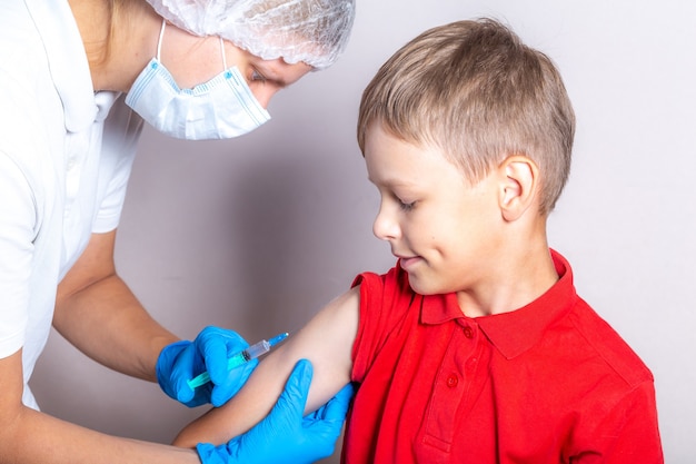 Фото Медсестра в маске и синих перчатках вводит вакцину мальчику через шприц.