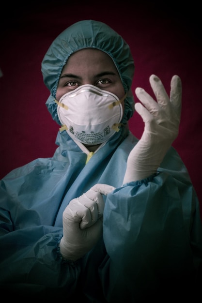 Фото Медсестра в маске и перчатках стоит на красном фоне.