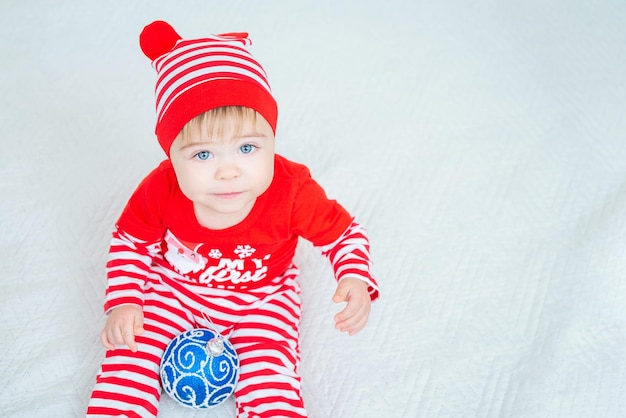 写真 赤と白のクリスマスの衣装を着た1歳のかわいい子供が青いクリスマスボールで遊ぶ