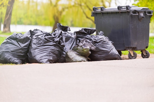 Фото Куча пластиковых мусорных мешков на обочине дороги рядом с пластиковым контейнером