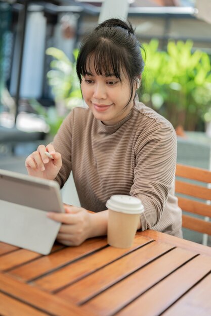 사진 카페에서 디지털 태블릿에서 일하는 긍정적 인 매력적인 아시아 여성