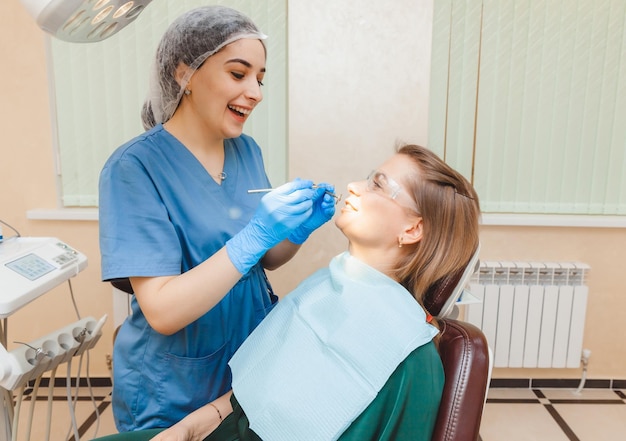 写真 健康診断の歯科医が女性の歯を調べている間、ポジティブな黒髪の女性が歯科医院に座っています。