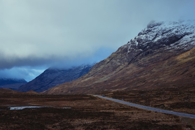 写真 グレンコーのスコットランドの高地を通って、雪を頂いたスコットランドの山々に続く道